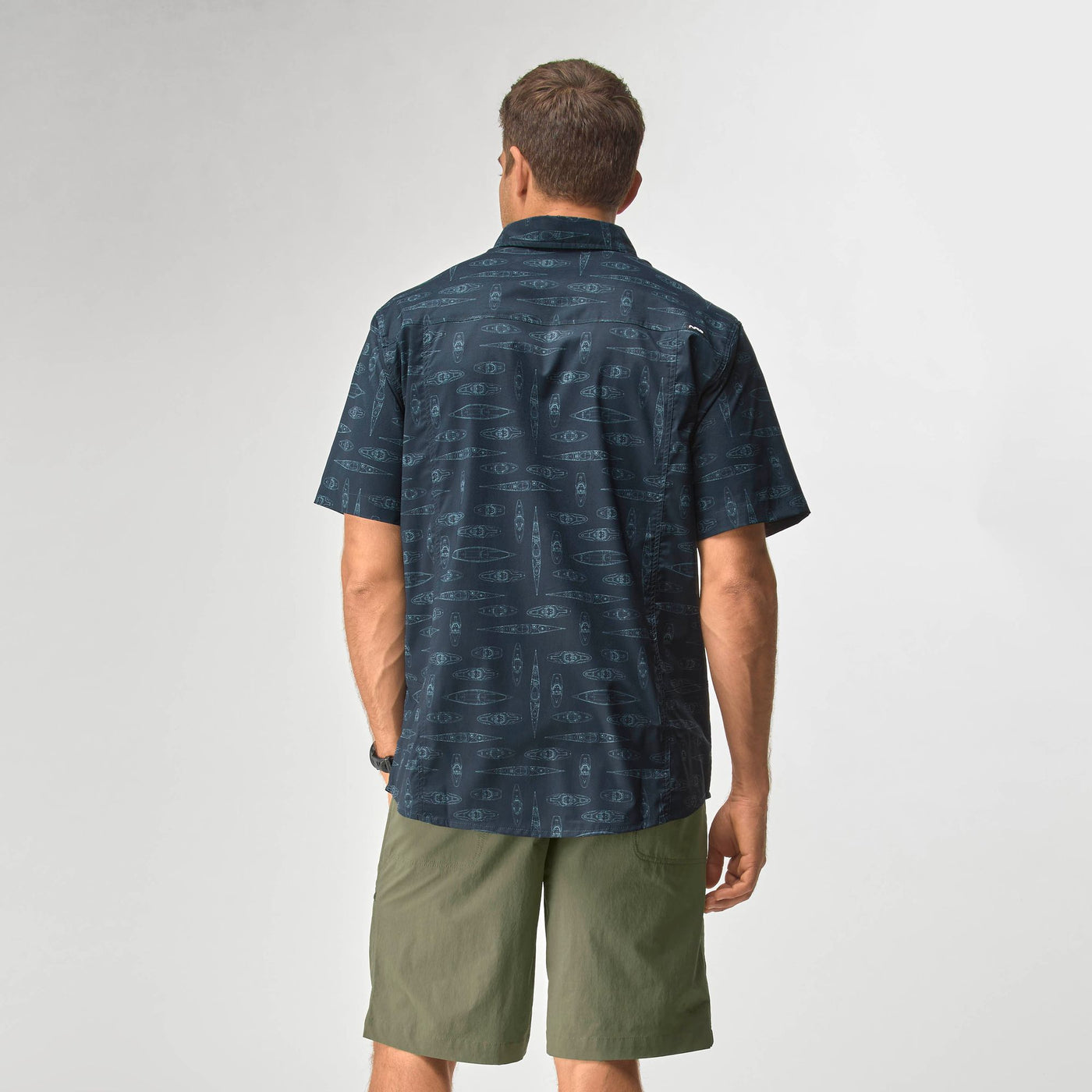 Man wearing NRS Men's Gear Shirt in navy blue with subtle pattern and olive green shorts, facing away from camera