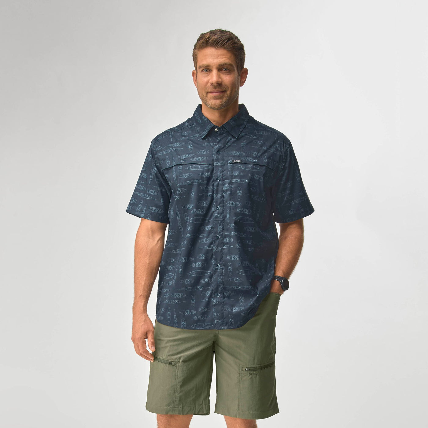 Man wearing a navy blue NRS Men's Gear Shirt with short sleeves and olive green shorts standing against a plain background
